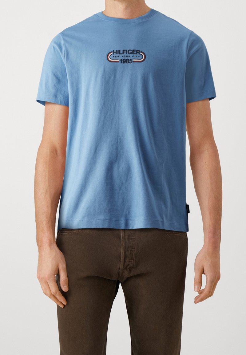 Jasnoniebieska koszulka z krótkim rękawem wykonana z bawełny, z graficznym logo w ciemnoniebieskim, czerwonym i białym kolorze z napisem "HILFIGER NEW YORK CITY 1985".
