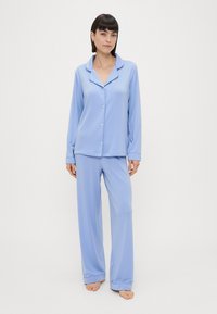 Conjunto de pijama azul claro com mangas longas, camisa com botões e calças de corte solto. Feito de tecido suave, apresentando um design de gola clássica.