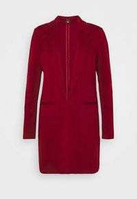 Robe blazer rouge avec une coupe slim, des manches longues, des revers en pointe et une fermeture éclair à l'avant. Elle dispose de deux poches avant et d'une texture lisse.