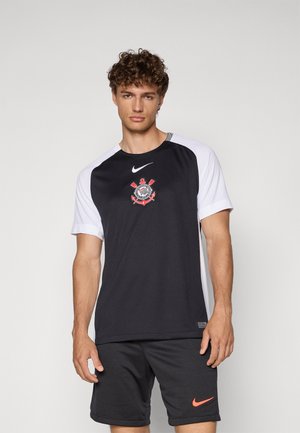 Černé sportovní tričko s bílými raglánovými rukávy, na hrudi s logem a Nike swoosh. V kombinaci se šedými šortkami.