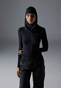 Svart atletisk bodysuit med høy krage og glidelås, kombinert med løse svarte bukser. Jevn tekstur, kroppsnær design.
