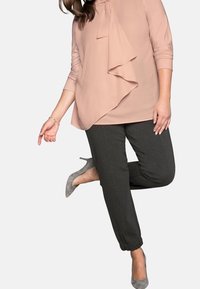 Rosa topp med kaskadruffel, trekvarts ärmar; mörkgrå tapered byxor; grå klackar som fulländar outfiten.