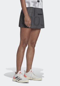 Svart idrotts kjol med geometriska mönster, parat med vita och korallfärgade sneakers. Har andningsbart tyg och en figurnära design.