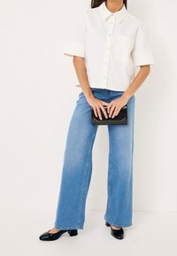 Vit kortärmad skjorta med knappstängning och bröstficka, ihopparad med ljusblå vida jeans och svarta lackläderblockklackskor.