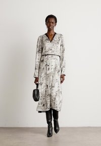 Long, loose-fitting dress with a black-and-white cityscape print, featuring a v-neck, long sleeves, a belt, and paired with knee-high black boots.