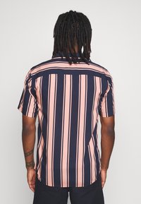 Camisa de manga corta con un diseño de rayas verticales en navy y rosa. Confeccionada en tejido ligero, cuenta con un dobladillo recto y una yugo en la parte posterior.