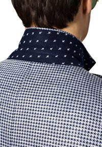 Koszula z kołnierzykiem w naprzemienne wzory granatowego i białego w kratkę houndstooth, z granatowym, teksturowanym kołnierzem ozdobionym małymi białymi wzorami kwiatowymi.