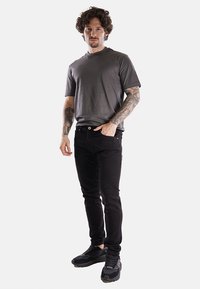 T-shirt grigio a maniche corte, jeans in denim neri e sneakers nere. L'outfit presenta un design semplice con una vestibilità regolare e linee pulite.