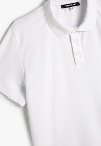 Polo blanca hecha de un tejido texturizado que presenta un cuello, una tapeta de tres botones y mangas cortas. Diseño sencillo sin patrones.