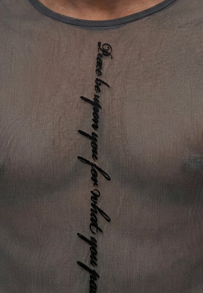 Διαφανές γκρι τοπ με μαύρο κάθετο κείμενο με πλάγια γράμματα που λέει «Έχω σπάσει σε πολλά εύθραυστα κομμάτια.»