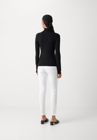 Black long-sleeve top with a mock neck, paired with white slim-fit pants and black block-heeled mules, displaying a sleek silhouette.
