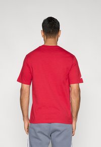 Κόκκινη κοντομάνικη βαμβακερή μπλούζα με στρογγυλή λαιμόκοψη, με απλό σχέδιο χωρίς μοτίβα ή διακοσμητικά, που φαίνεται από πίσω.