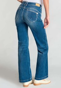 Jeans a palazzo in denim blu con vita media, dettaglio di cucitura, cinque tasche e una texture liscia. Completati con un'etichetta in pelle con il marchio.