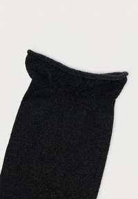 Μαύρο κορδωτό πάνω μέρος κάλτσας με μια ελαφρώς φραμπαλά λεπτομέρεια στην άκρη σε λευκό φόντο.