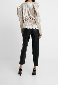 Metallic pleated blouse with puffed sleeves and elasticated waist, paired with fitted black leather trousers and high-heeled shoes.