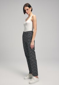 Zwarte broeken met een wit stippenpatroon, met een hoge taille en een rechte pijp. Gecombineerd met een aansluitend wit tanktop en witte sneakers.