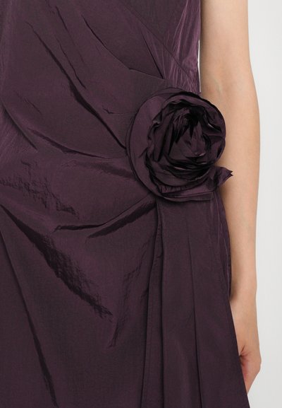 Purple fabric dress featuring a textured, crinkled design and a large, rosette detail on the side, creating a dynamic silhouette.