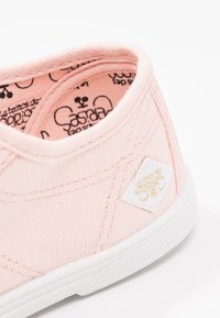 Gros plan sur le talon d'une chaussure de toile rose clair avec semelle en caoutchouc blanche et tissu intérieur imprimé.