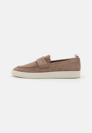 Chaussures slip-on en suède marron clair avec une semelle extérieure crème. Présente une bande proéminente sur le dessus et une languette à l'arrière.