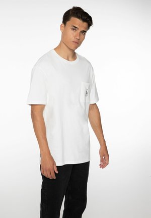 T-shirt en coton blanc avec un col rond et des manches courtes. Présente une poche sur la poitrine gauche avec un logo imprimé. Assorti à un pantalon noir.