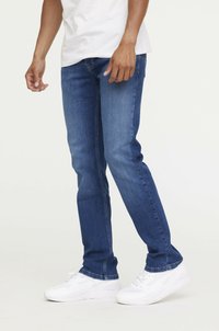 Jean en denim bleu avec une coupe slim, présentant un léger délavage, un design à cinq poches et des coutures claires ; assortis avec des baskets blanches.