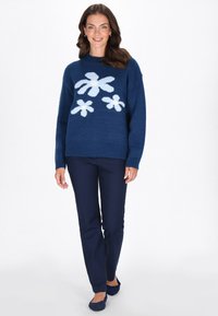 Marineblauer Strickpullover mit floralem Muster in Hellblau, rundem Ausschnitt und gerippten Bündchen, kombiniert mit marineblauen Hosen und blauen Ballerinas.
