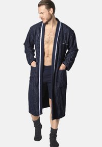 Navy blue waffle-textured bathrobe with contrasting white trim, two front pockets, and a relaxed fit, paired with dark shorts and socks.