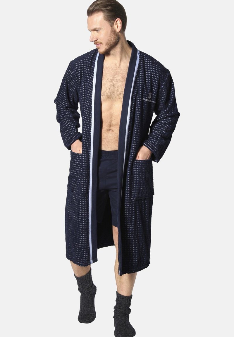 Navy blue waffle-textured bathrobe with contrasting white trim, two front pockets, and a relaxed fit, paired with dark shorts and socks.