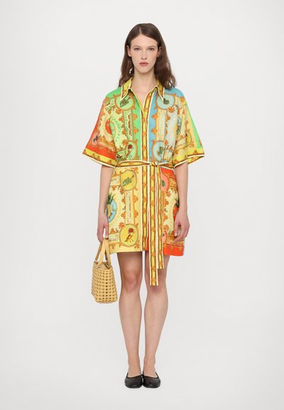 Colorful short dress with a collar, featuring a pattern of intricate designs in green, orange, and yellow. Paired with a woven yellow bag.