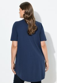 Námořnická modrá tunika s krátkým rukávem kulatým lemem a měkkou texturou, s uvolněným střihem a minimálními detaily.