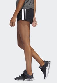 Čierne športové šortky s bielymi bočnými prúžkami, kombinované s čierno-bielymi teniskami s vzorom. Materiál vyzerá byť ľahký a priedušný.