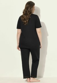 Completo pigiama nero composto da una maglietta a maniche corte e pantaloni con bordino in pizzo all'orlo. Tessuto morbido e vestibilità comoda per il massimo comfort.