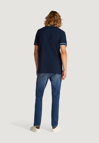 Camisa polo navy con rayas blancas y rosas en las mangas, combinada con jeans azules y zapatillas blancas. Mangas cortas y corte relajado.