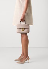 Sac à main en cuir rose clair avec un design structuré, des accessoires en métal doré et une poignée supérieure. La robe a un motif à carreaux beige.
