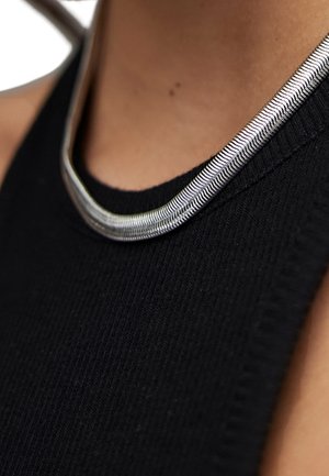 Collier argenté à torsades porté sur un haut sans manches noir à torsades, visible sur le cou et le haut de la poitrine d’une personne.