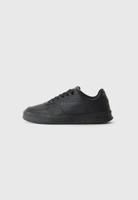 Chaussure de sport noire au design épuré avec un dessus en synthétique lisse, semelle en caoutchouc plate, bout rond et fermeture à lacets avec détail de logo sur le côté.