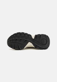 Soletta in gomma nera con un profondo disegno del battistrada, caratterizzata da una combinazione di forme angolari e arrotondate. Il design include un accento beige medio.