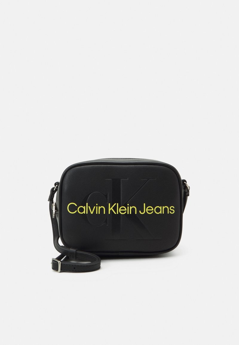 Borsa a tracolla nera realizzata in morbida ecopelle, con un logo impresso e un testo giallo brillante "Calvin Klein Jeans". Cinghia regolabile.