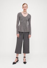 Sivi pleteni peplum top s dugim rukavima, uparen sa sivim hlačama širokih nogavica i crnim cipelama s špicastim vrhom i trakastim detaljima. Srebrni ogrlica.