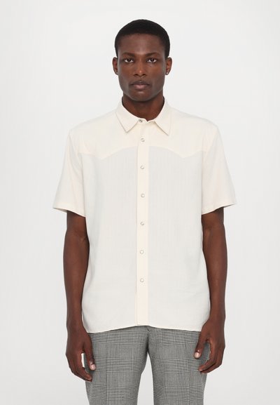 Chemise à manches courtes en tissu blanc cassé avec un léger éclat, dotée d'une couture de dos et de fines rayures verticales.