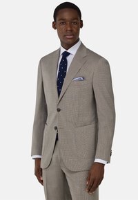 Traje gris claro con un patrón de cuadros, corte entallado y dos botones. Combinado con una corbata de lunares azul y un pañuelo de bolsillo a rayas.