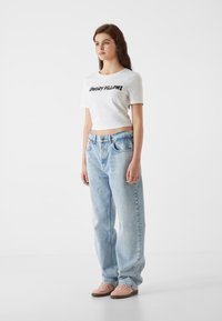 Camiseta blanca corta con el texto "COWBOY PILLOWS", jeans ajustados de mezclilla azul claro y zapatillas rosas. Diseño sencillo con estilo casual.