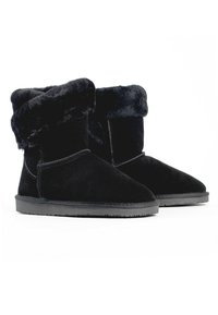 Botas de ante negras con un puño de piel sintética doblado, suela plana de goma negra, punta redondeada y detalles de costura visibles a lo largo de las costuras.