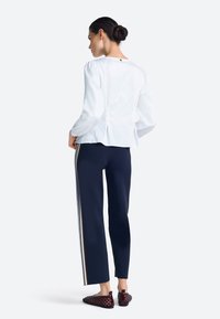 Top blanco de manga larga con dobladillo peplum, combinado con pantalones azul marino con franjas laterales y zapatos rojos tejidos sin cordones. Vista trasera.