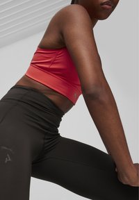 Piros sportmelltartó, testhez simuló dizájnnal és logóval, magas derekú fekete leggings-szel párosítva, amelyek diszkrét márkázással és sima textúrával rendelkeznek.