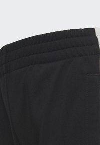 Un short de sport noir présente une taille élastique avec un tissu texturé. Le design comprend une poche sur le côté et des accents blancs contrastants.