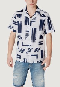 Korte mouwen, witte overhemd met knopen, versierd met een marineblauw penseelstreek geometrisch patroon. Draagt bij verwassen blauwe denim shorts.