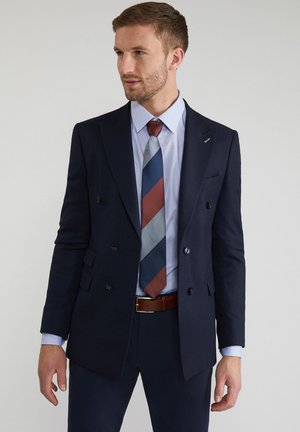 Navy blue, dwurzędowa marynarka uszyta z teksturowanej tkaniny, noszona na jasnoniebieskiej koszuli i wzorzystym krawacie w czerwone, niebieskie i srebrne paski.