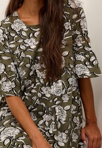 Olivengrünes Kleid mit einem floralen Druck in Schwarz und Weiß, ausgestattet mit kurzen Rüscheärmeln und einem lässigen, fließenden Design.
