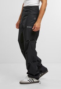 Zwarte cargo broek met een losse pasvorm, voorzien van zijzakken, verstelbare boorden en een wit logo aan de voorkant. Gemaakt van duurzame stof.